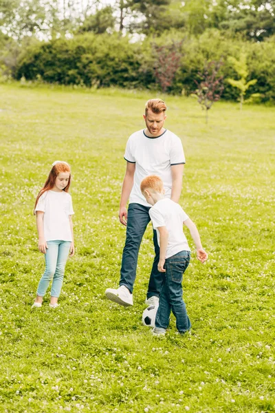 Батько з чарівними дітьми грає з футбольним м'ячем у парку — стокове фото