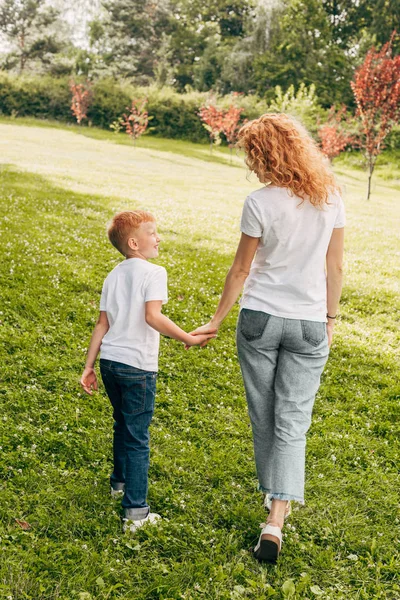 Back view of happy mother and son holding hands and walking together in park — Stock Photo