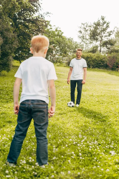 Батько і син грають з футбольним м'ячем на зеленому газоні в парку — стокове фото