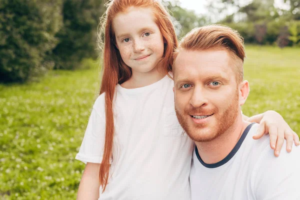 Feliz pelirroja padre e hija sonriendo a la cámara en el parque - foto de stock