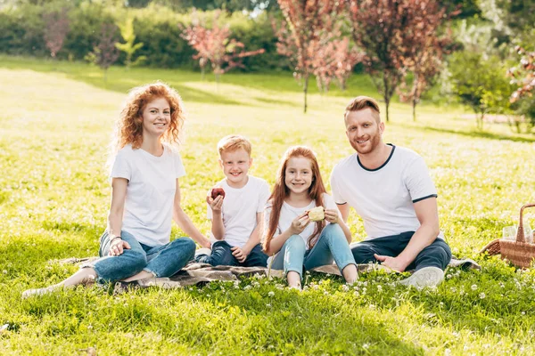 Heureux famille souriant à la caméra tout en étant assis ensemble au pique-nique dans le parc — Photo de stock