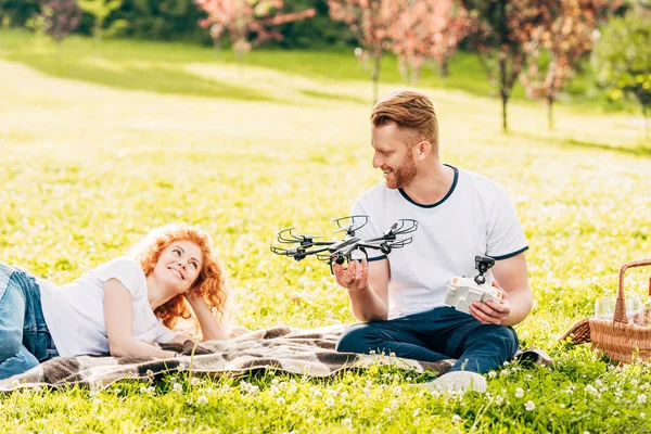 Feliz pelirroja pareja jugando con drone en picnic en parque - foto de stock