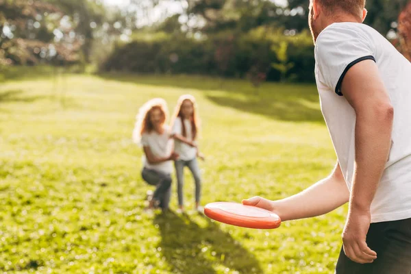 Cropped shot of father throwing flying disk to mother and daughter in park — Stock Photo