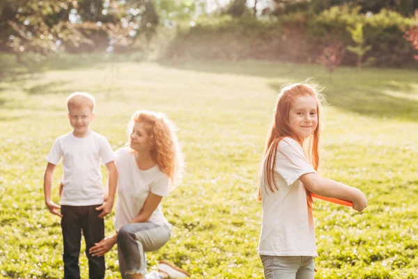 Happy child playing with flying disk while mother and brother resting behind in park — Stock Photo