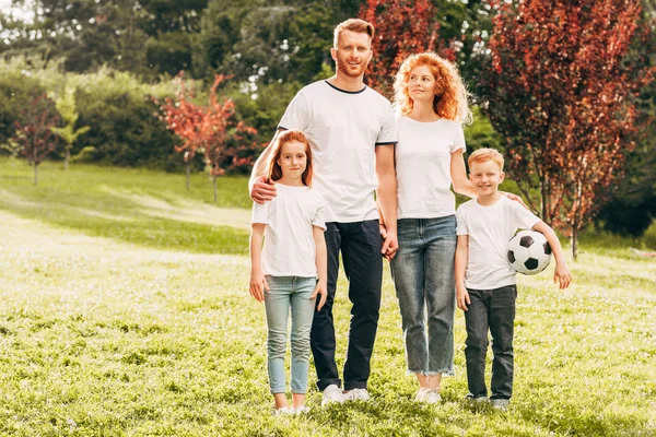 Familia feliz con dos niños sosteniendo la pelota de fútbol y sonriendo a la cámara en el parque - foto de stock