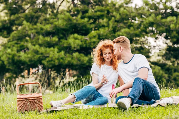 Glückliches Paar trinkt Wein, während es auf Plaid beim Picknick im Park sitzt — Stockfoto