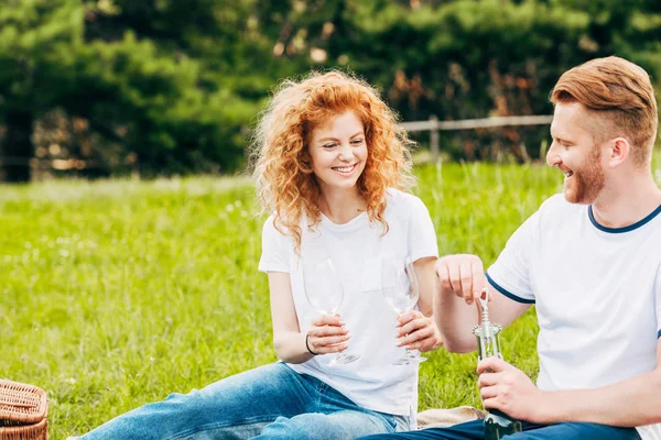 Happy couple opening bottle of wine at picnic in park — Stock Photo