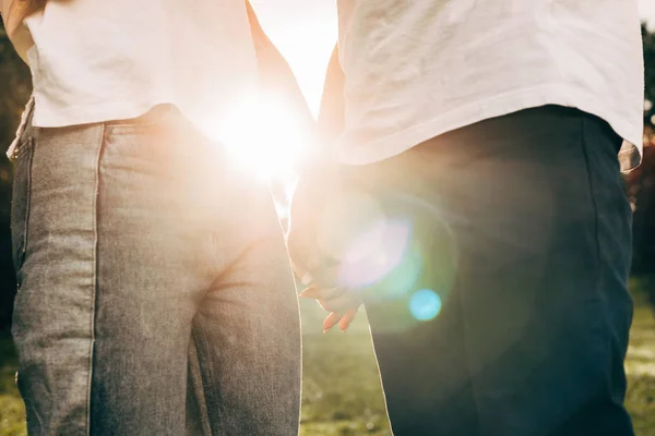 Recortado disparo de joven pareja cogido de la mano mientras de pie juntos en el parque al atardecer - foto de stock