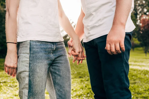 Schnappschuss von jungem Paar, das sich Händchen hält, während es im Park zusammensteht — Stockfoto