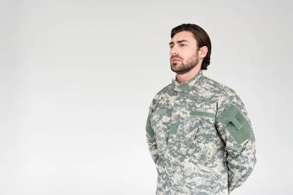 Vista laterale di soldato barbuto fiducioso in uniforme militare guardando lontano su sfondo grigio — Foto stock