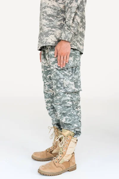 Vista parziale di soldato maschile in abiti mimetici e stivali su sfondo grigio — Foto stock
