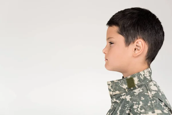 Vista laterale del bambino in uniforme militare guardando lontano su sfondo grigio — Foto stock