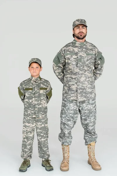 Padre e hijo en uniformes militares mirando a la cámara sobre fondo gris - foto de stock