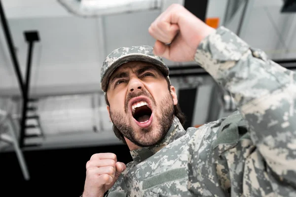 Low angle view of emotional soldier in military uniform with blurred backdrop — Stock Photo