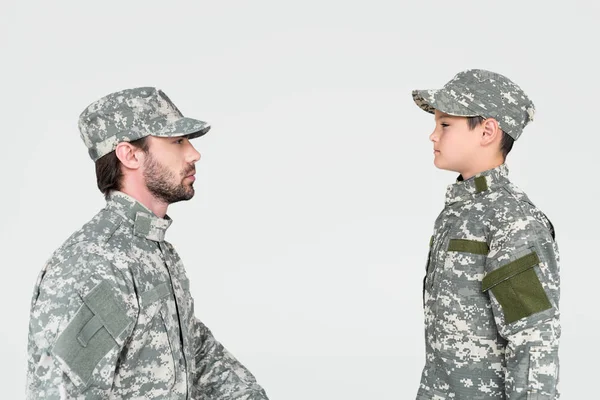 Seitenansicht von Soldat und Sohn in Militäruniformen, die sich isoliert auf grau anschauen — Stockfoto