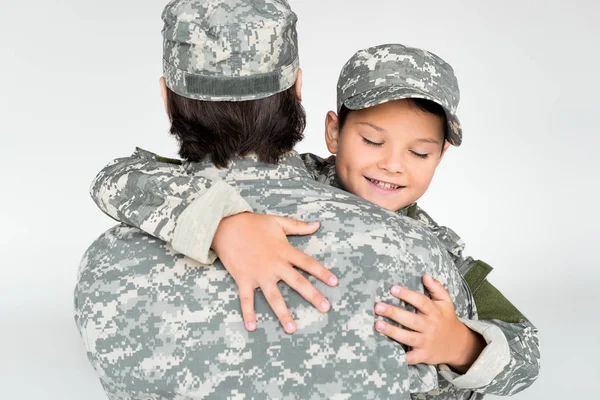 Partial view of father and smiling son in military uniforms hugging each other on grey background — Stock Photo