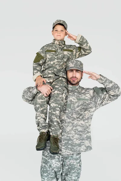 Soldier holding son in military uniform on shoulder and saluting isolated on grey — Stock Photo