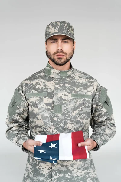 Retrato de soldado masculino en uniforme militar con bandera americana en las manos sobre fondo gris - foto de stock
