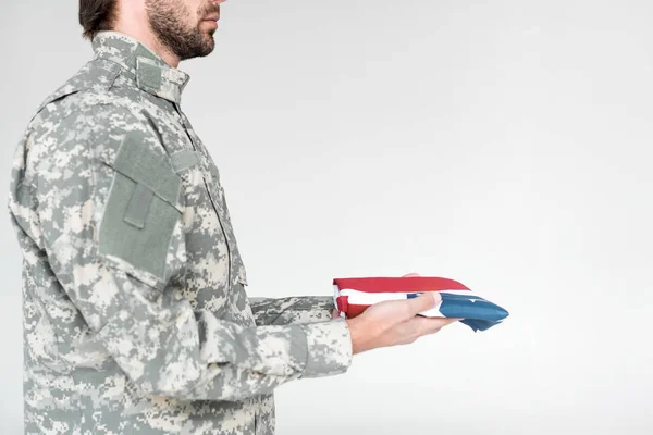 Vista parcial del soldado en uniforme militar con bandera americana en las manos sobre fondo gris - foto de stock