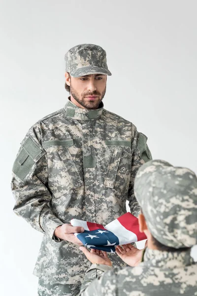 Vista parcial de soldado dando bandera americana doblada a niño en ropa de camuflaje sobre fondo gris — Stock Photo