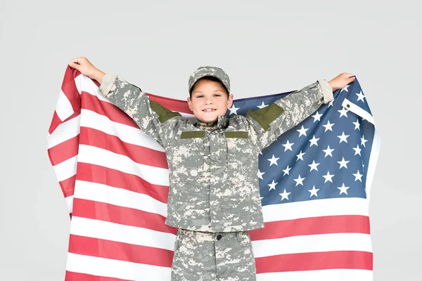 Retrato de niño alegre en uniforme militar con bandera americana aislado en gris - foto de stock