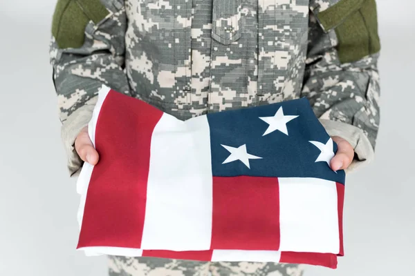 Cropped shot of kid in military uniform holding folded american flag in hands isolated on grey — Stock Photo