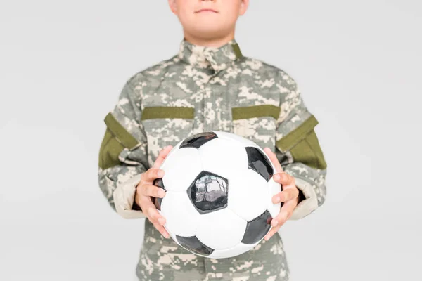 Vista parziale del bambino in uniforme militare con pallone da calcio in mano isolato su grigio — Foto stock