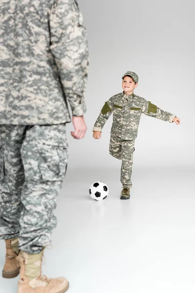 Vista parziale di padre e figlio in uniforme militare che giocano a calcio su sfondo grigio — Foto stock