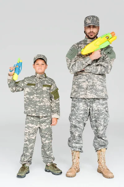 Padre e hijo en uniformes militares con pistolas de agua de juguete sobre fondo gris - foto de stock