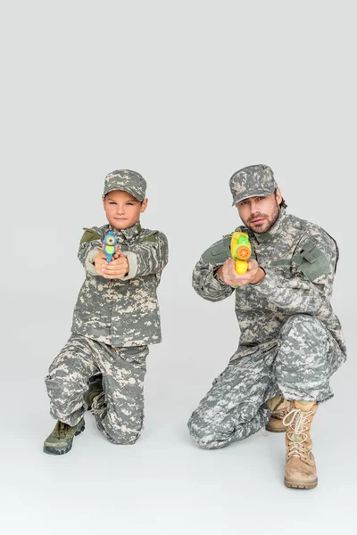 Padre e hijo en uniformes militares con pistolas de agua de juguete sobre fondo gris - foto de stock