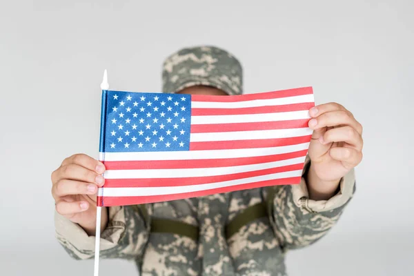 Obscured view of kid in camouflage clothing showing american flagpole in hands isolated on grey — Stock Photo