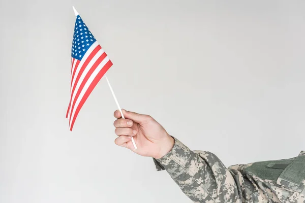 Vista parcial de niño en ropa de camuflaje sosteniendo asta de bandera americana en mano aislado en gris - foto de stock