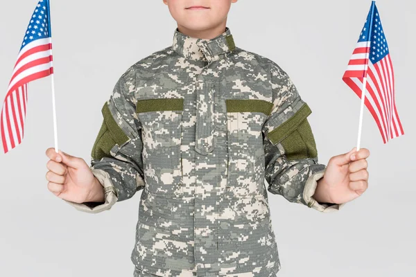 Cropped shot of child in military uniform with american flagpoles in hands isolated on grey — Stock Photo