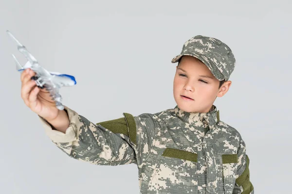Retrato de niño pequeño en uniforme militar con avión de juguete en mano aislado en gris - foto de stock
