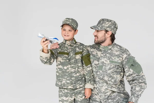 Retrato de padre e hijo en uniformes militares con avión de juguete aislado en gris - foto de stock