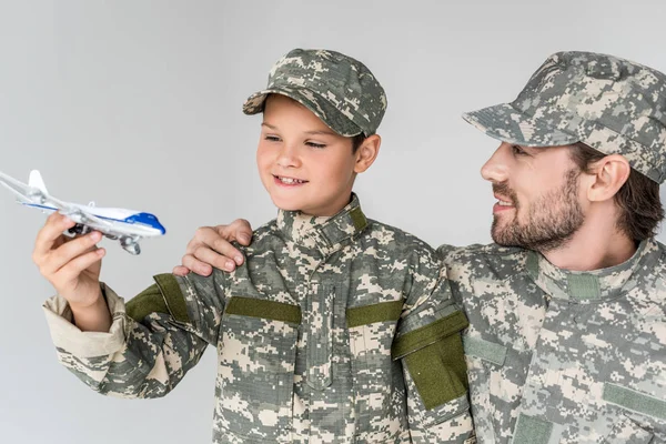 Retrato de padre e hijo en uniformes militares con avión de juguete aislado en gris - foto de stock