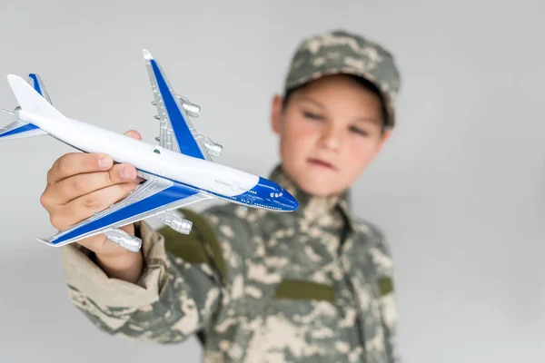 Selective focus of little boy in military uniform with toy plane in hand isolated on grey — Stock Photo