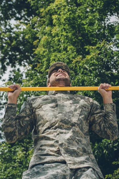 Baixo ângulo de visão do soldado em uniforme militar puxando-se na barra transversal — Fotografia de Stock