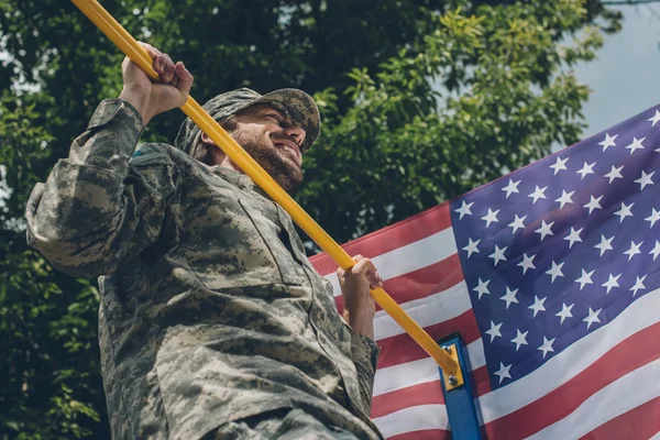 Vue à angle bas du soldat se tirant vers le haut sur la barre transversale avec drapeau américain sur fond — Photo de stock