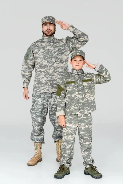Familia en uniformes militares saludando y mirando a la cámara sobre fondo gris - foto de stock