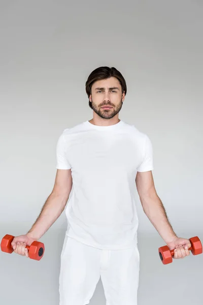 Портрет человека в белой рубашке с красными гантелями в руках на сером фоне — стоковое фото