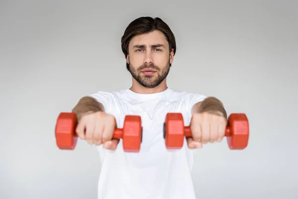 Retrato de hombre de camisa blanca con mancuernas rojas en las manos ejercitándose sobre fondo gris - foto de stock