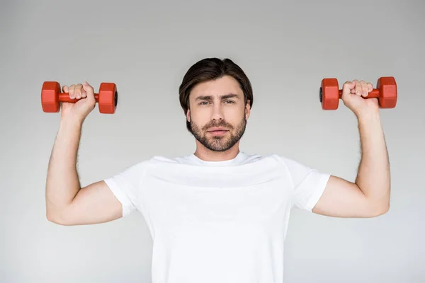 Portrait of man in white shirt with red dumbbells in hands exercising on grey backdrop — Stock Photo