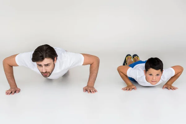 Pai e filho fazendo flexões juntos em fundo cinza — Fotografia de Stock