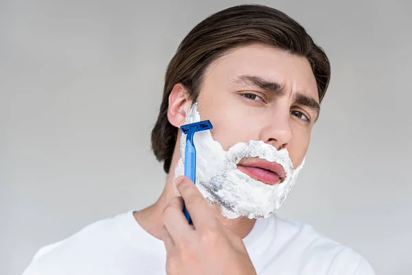 Retrato de homem atraente com espuma no rosto e barba de barbear barbear no fundo cinza — Fotografia de Stock