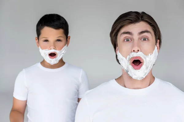Портрет шокованого батька і сина з піною для гоління на обличчях ізольовані на сірому — стокове фото