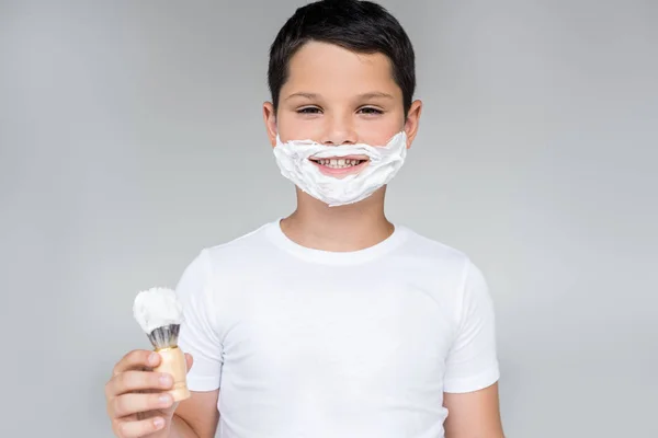 Portrait de préadolescent souriant avec brosse à la main et mousse à raser sur le visage isolé sur gris — Photo de stock