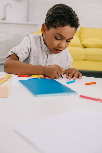 Porträt eines afrikanisch-amerikanischen Jungen zeichnet Bild mit Buntstiften am Tisch im Klassenzimmer — Stockfoto