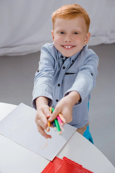 Allegro bambino in età prescolare capelli rossi con matite seduto a tavola con carta per disegnare in classe — Foto stock