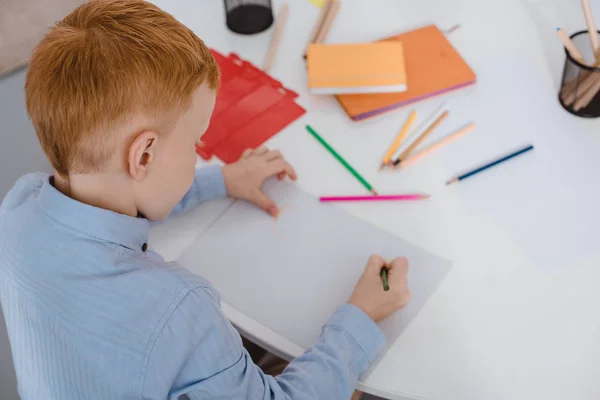 Vue grand angle de cheveux roux garçon dessin image avec crayons à la table — Photo de stock